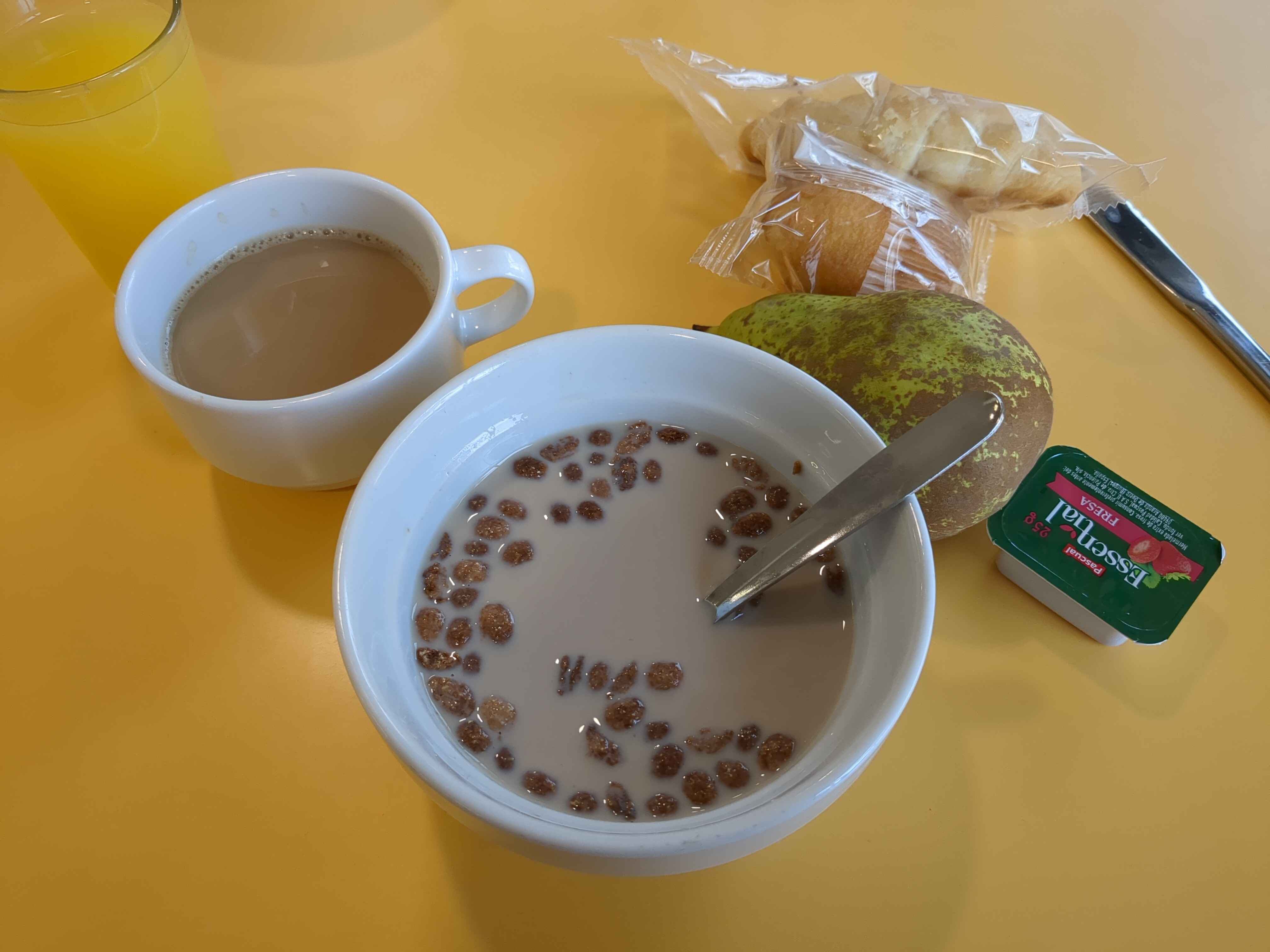 hostel breakfast of cereal, croissant, pear, madeline, and coffee