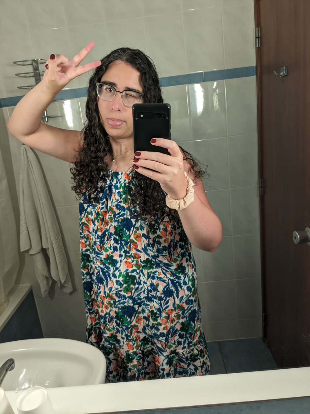 katey smiling in a bathroom mirror. she is holding a peace sign in front of her forehead.